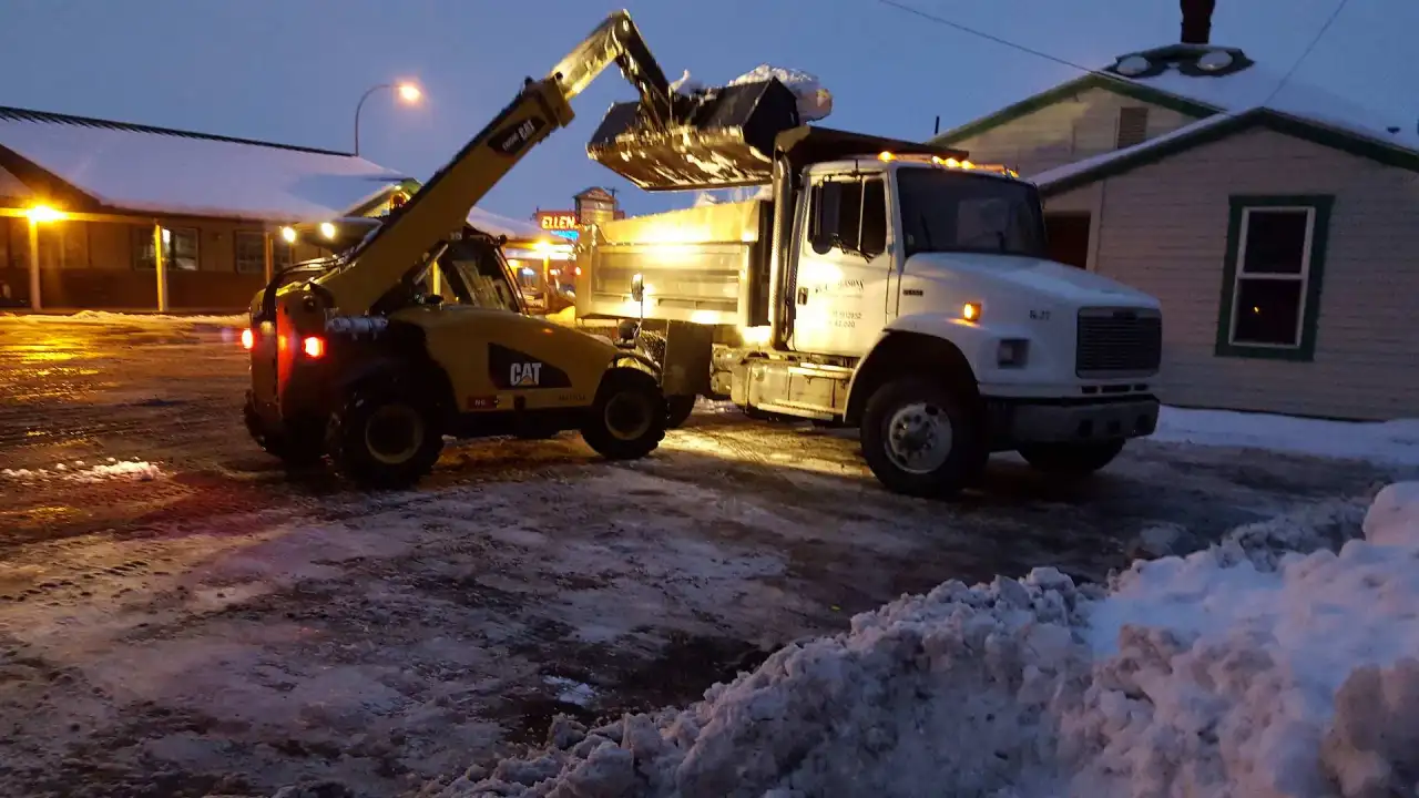 Crystal Clear loader filling a dump truck with snow at dusk