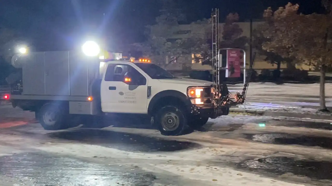 De-icing truck with a front spray boom on a parking lot at night